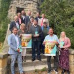 Voller Vorfreude auf das Parkfest 2025: Auf der Treppe des Belvederes zeigen Stadt und Sponsoren mit Plakaten und Flyern, was die Gäste am 2. August erwartet – ein Tag voller Musik, Begegnung und Le-bensfreude im Herzen der Spiegelsberge.